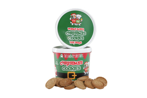 A tub of The Bakery Brothers Christmas Cookies for Dogs, with several round golden-brown cookies scattered in front on a clean white background.