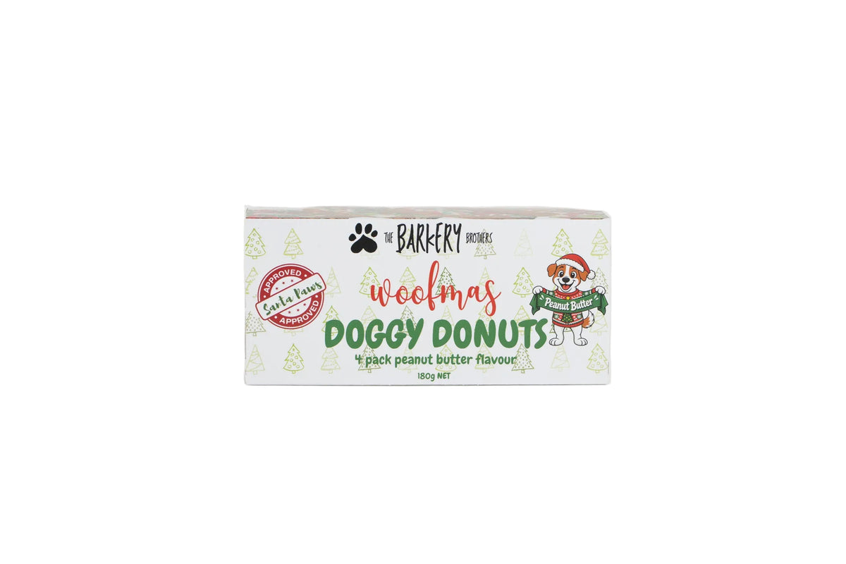 A rectangular box of 'The Barkfery Doggy Donut' Christmas themed dog treats, featuring a white background with green pine tree illustrations, red and green text, and a cartoon dog wearing a Santa hat and sweater.